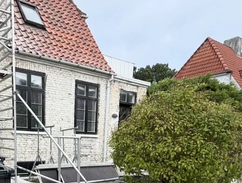 Hvid facade med mørke vinduer og stillads ved huset